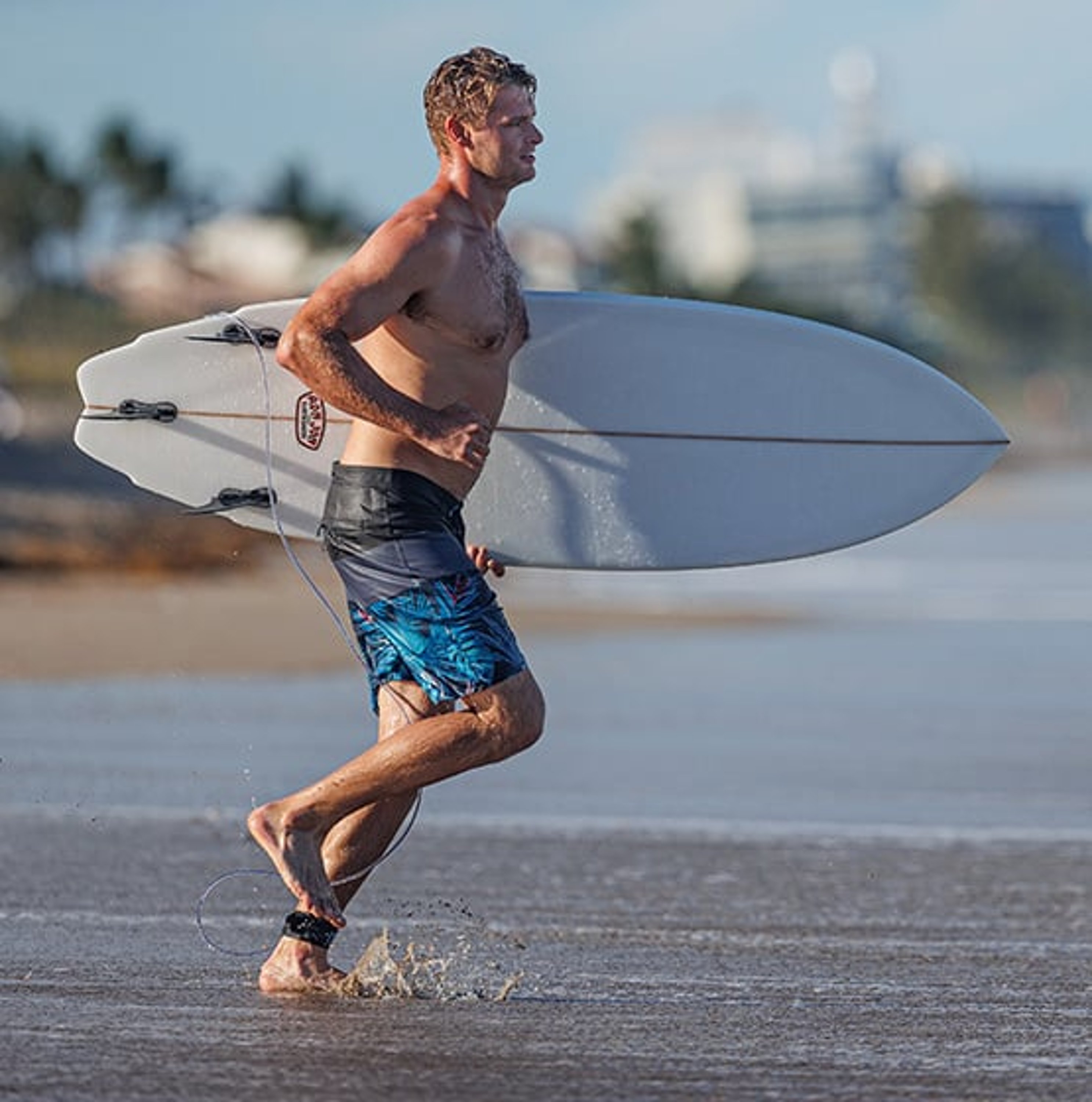 guy running on the beach toward the water carrying a surfboard wearing Ron Jon Royal Palm boardshorts